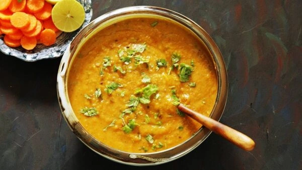 Creamy Punjabi dal tadka garnished with fresh coriander in a metal bowl, served with sliced carrots and lemon.