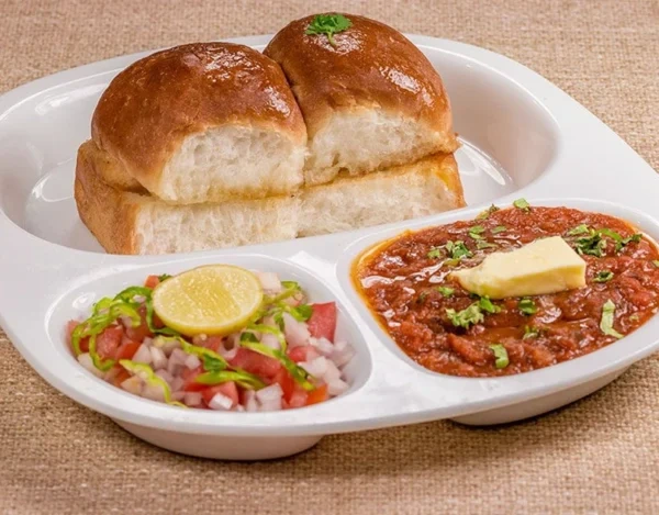 Spicy Pav Bhaji topped with butter and served with soft buns, onions, and lemon at Punjabi Zaaika restaurant.