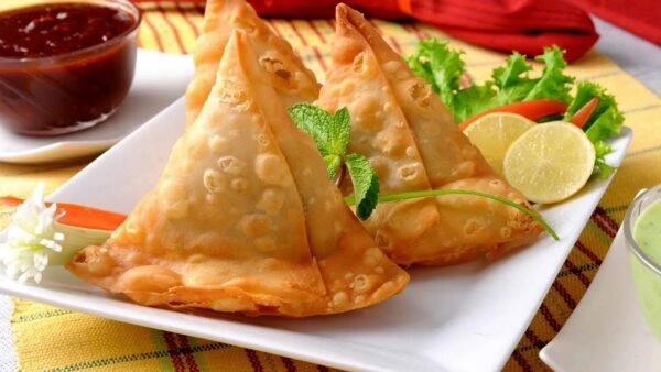 Crispy golden Punjabi samosas served on a white platter with mint leaves, lemon slices, and dipping chutneys.