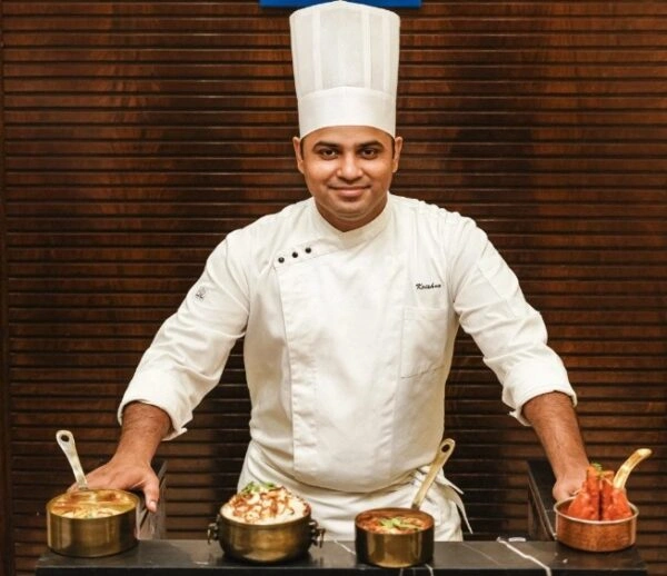 Professional Indian chef in a white uniform presenting authentic North Indian dishes at Punjabi Zaaika restaurant.