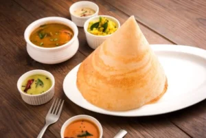 Cone-shaped crispy dosa served on a white platter with sambar and traditional chutneys at Punjabi Zaaika restaurant.